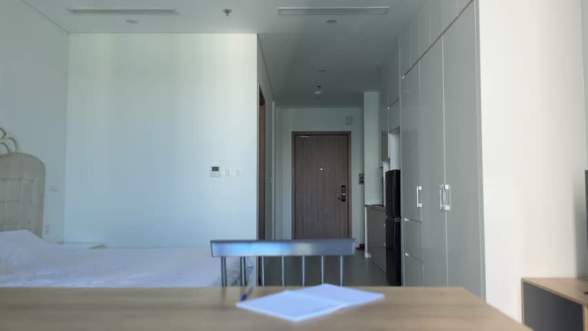 A young guy, dyed stylish blond in a blue t-shirt sits at a desk in a bright interior and writes in a notebook. He doesn