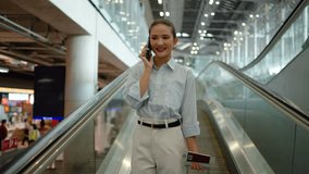 A asian businesswoman exudes confidence and happiness as she navigates an escalator while chatting on her mobile phone in a vibrant airport lobby, enjoying a networking moment. - Powered by Shutterstock - Get 15% off with code: PIKWIZARD15