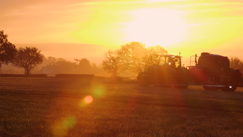 Tractor farms the land against a sunset background.