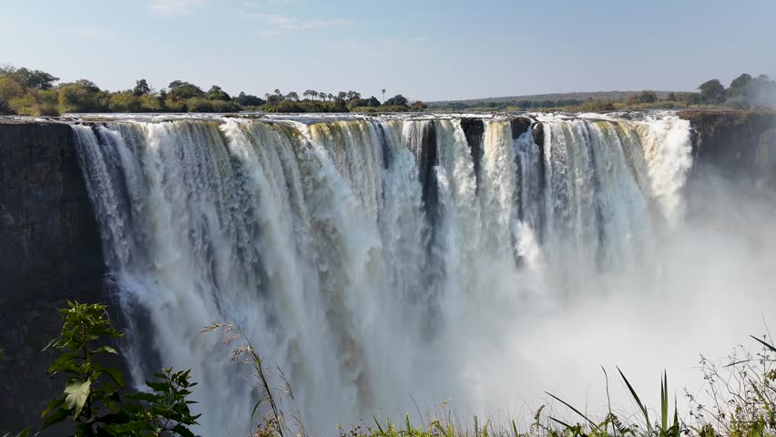 Scenic Water Falls In Victoria Falls Matabeleland North Zimbabwe. Rainbow Forming Over Waterfalls With River In Background. Landscape Dramatic Clouds Waterfall Tropical. Mountain Panoramic.