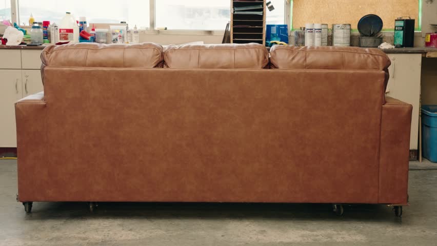 Brown leather sofa back in workshop as technician steps behind for pose
