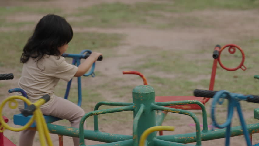 toddler girl having fun while playing on carousel at outdoor playground