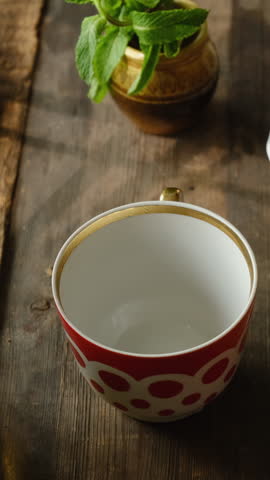 Vertical video. Afternoon tea time. Hands pouring brewed herbal green tea with fresh mint from teapot. 