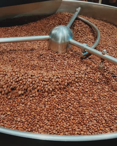 Coffee roaster machine at coffee roasting process. Mixing coffee beans. Roasted spinning cooler professional machines and fresh brown coffee beans movement close-up dark video at factory.