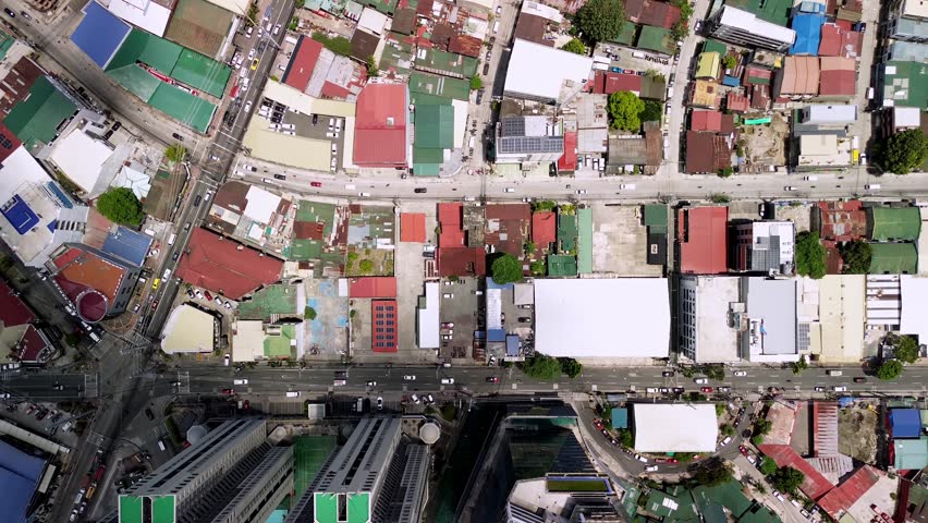 Drone captures a top-down view of Makati streets as moving clouds cast dynamic shadows across buildings and roads, creating a stunning urban light play in midday sun.