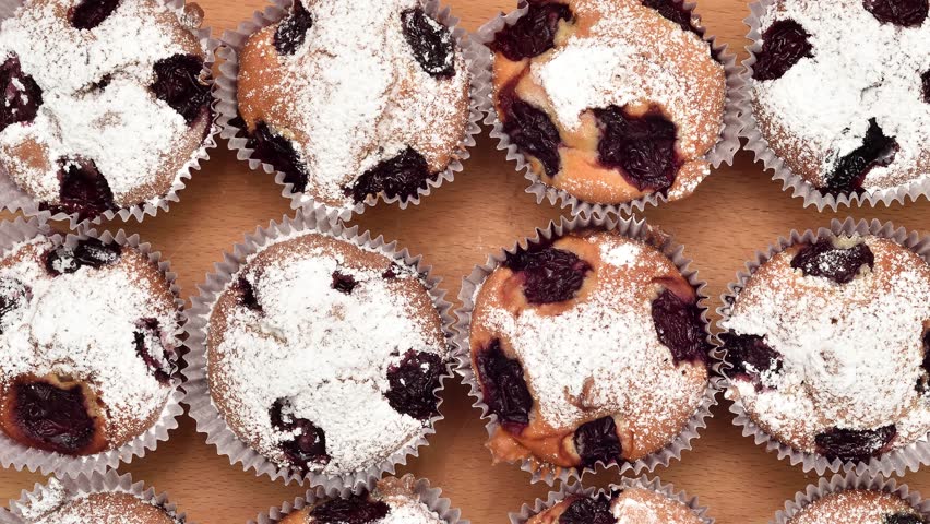 Homemade muffins with sour cherry sprinkled with powdered sugar on the wooden board. Close-up. Top view. Panning shot.