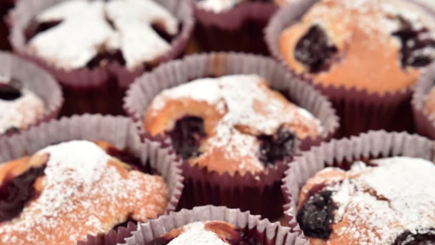Homemade muffins with sour cherry sprinkled with powdered sugar on the wooden board. Close-up. Selective focus. Tilt down shot.