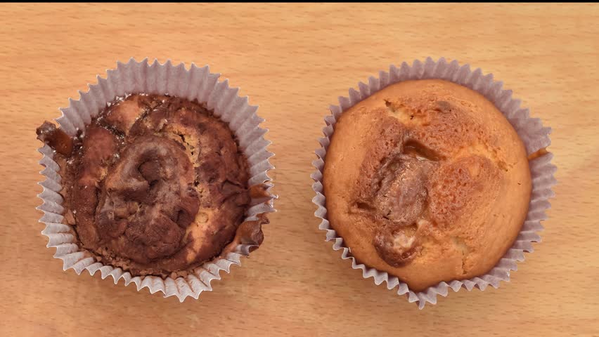 Different homemade muffins with chocolate, cocoa powder, jam and sour cherry sprinkled with powdered sugar on the wooden board. Close-up. Tilt down shot. 