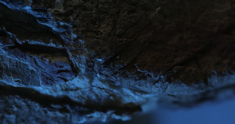 Close-up of dark rock surface with vivid blue lighting and layered texture