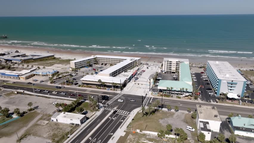 Daytona Beach, Florida with waves from the Atlantic Ocean, vehicles, hotels and people on the beach with drone video moving in a circle.