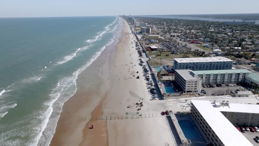 Daytona Beach, Florida with waves from the Atlantic Ocean, vehicles, hotels and people on the beach with drone video moving forward.