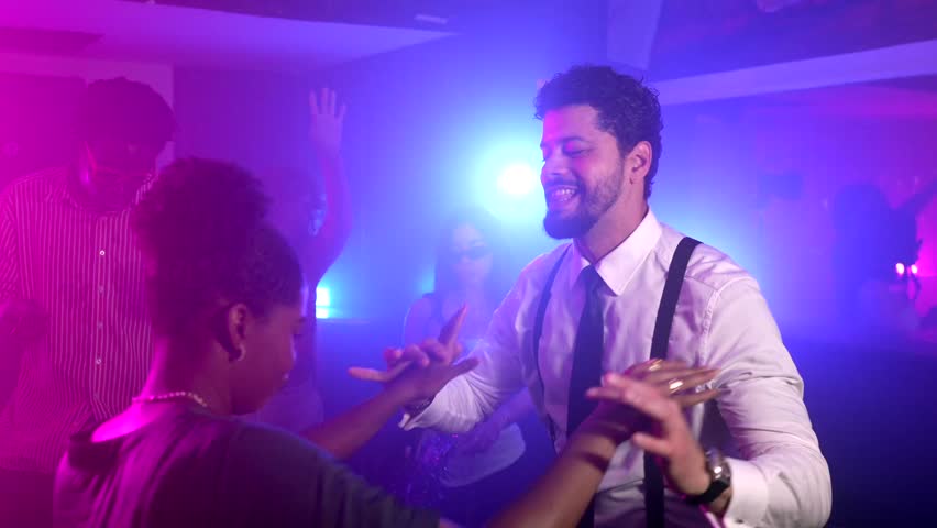 Energetic romantic couple dancing closely together, sharing joyful connection under vibrant multicolored nightclub illumination with dynamic festive atmosphere