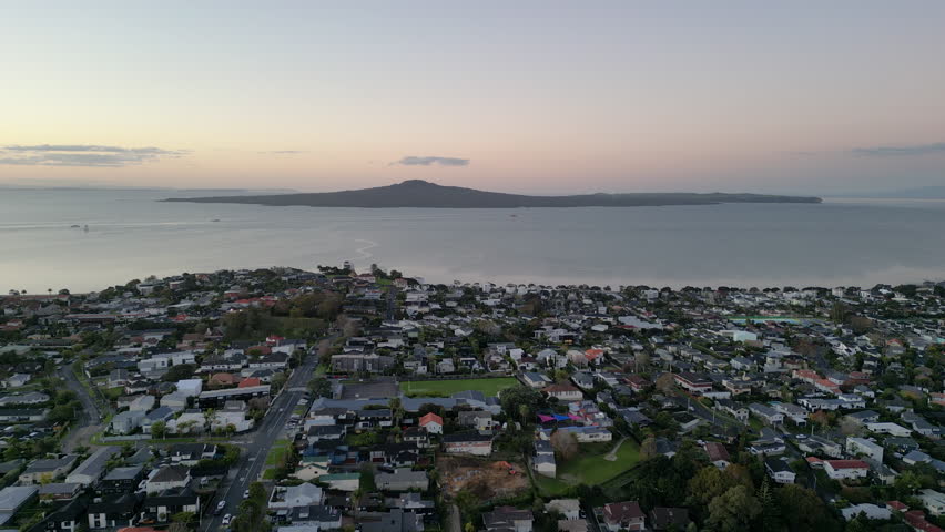 Drone view of Auckland coastline and suburbs with Mt Rangitoto on the horizon at sunset, New Zealand