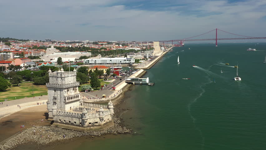 Aerial drone shot of Belem Tower and the 25 de Abril suspension bridge over the Tagus River in Lisbon, showcasing the iconic landmarks and scenic waterfront