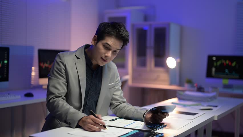 A man in a suit is sitting at a desk with a tablet in front of him. He is writing on a piece of paper with a pen. The scene suggests a professional setting, possibly in an office or a conference room - Powered by Shutterstock - Get 15% off with code: PIKWIZARD15