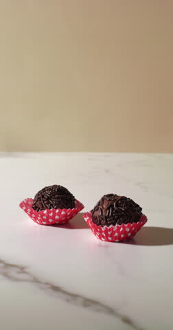 Close-up of a hand gently picking up a chocolate truffle with sprinkles from a red polka dot paper cup. The minimal marble background and bright lighting create a clean, elegant dessert presentation.