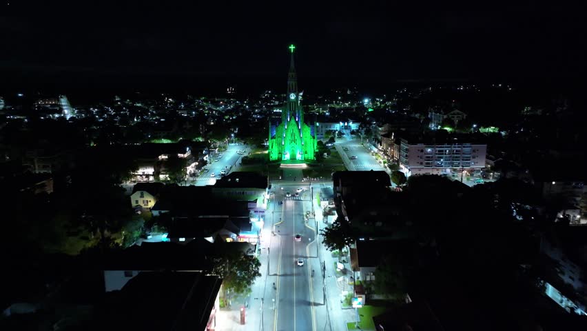 Illuminated Church In Canela Rio Grande Do Sul Brazil. Bird Eye View Of Church Standing Tall Amidst Beautiful Scenery. Building Clouds Sky Downtown Cityscape. Night Outdoors Panning Wide.