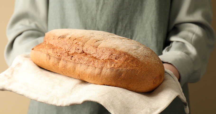 Woman with loaf of bread on light background, closeup
