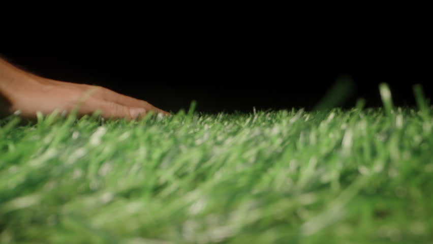 Close-Up of Hand Gently Stroking Artificial Green Grass with Visible Contact and Tactile Interaction Against Dark Background Concept Human Touch and Synthetic Nature.