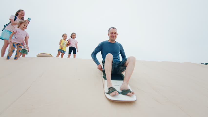 Family sandboarding. Man glides with kid down the sand dune