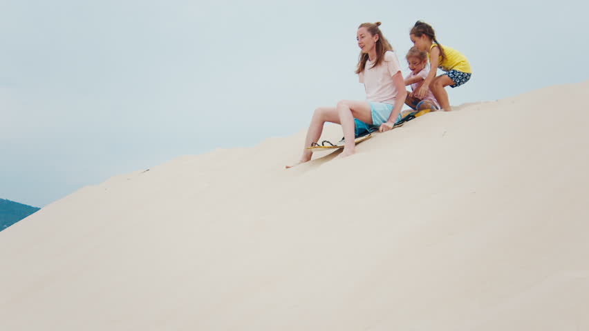 Family sandboarding. Woman glides down the sand dune with all the family watching her