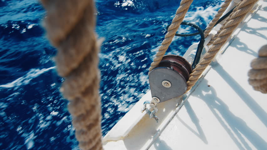 Ropes and deck and deep blue sea view from the moving sailing vessel in the open sea