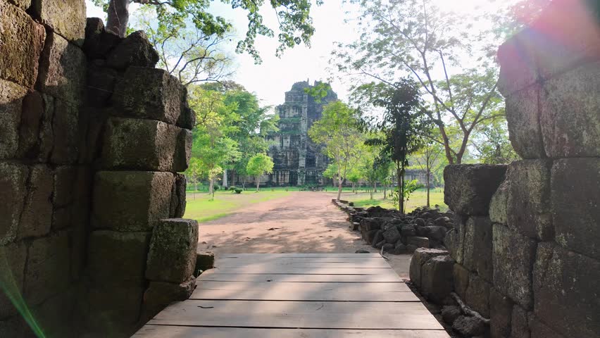 walkthrough shot moves along a path, framed by dense jungle, before unveiling the towering stone pyramid of Prasat Tom at Koh Ker, Cambodia.