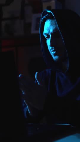 Anonymous hacker browsing the dark web on laptop in dimly lit room symbolizing illegal activity and cybercrime