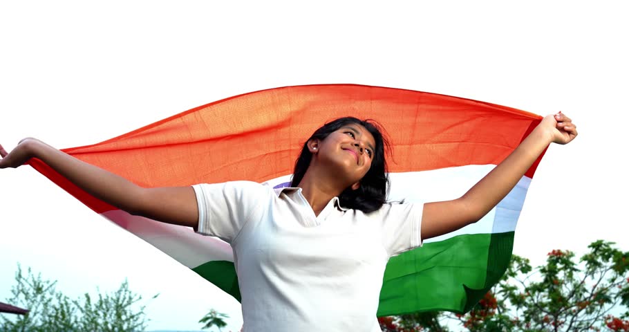 Holding Indian Flag, Cheerful Teenage Girl Standing in Open Air as Tricolour Flutters in the Wind, Happy Asian Child Displaying National Pride and Patriotism Under Blue Sky with Joyful Expression