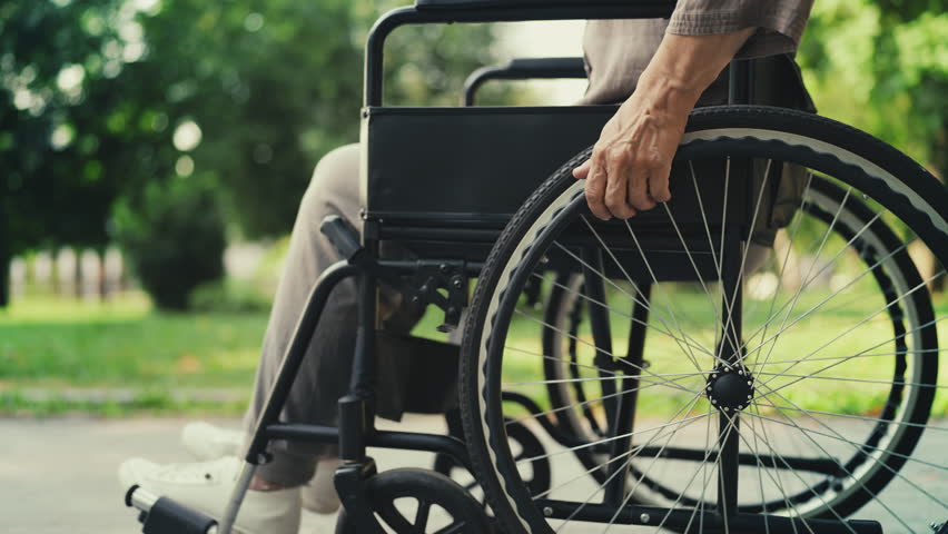 Senior woman with disability using manual wheelchair in park, reduced mobility