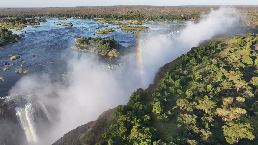 Rainbow In Waterfall In Victoria Falls Matabeleland North Zimbabwe. Experience The Majestic Flow Of Waterfalls With Lush Greenery. Nature Dramatic Clouds Mountain Canyon.