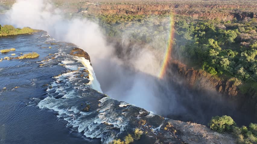 Water Fall Rainbow In Victoria Falls Matabeleland North Zimbabwe. Rainbow Forming Over Waterfalls With River In Background. Landscape Dramatic Sky Waterfall Tropical. Landscape Powerful Flow.