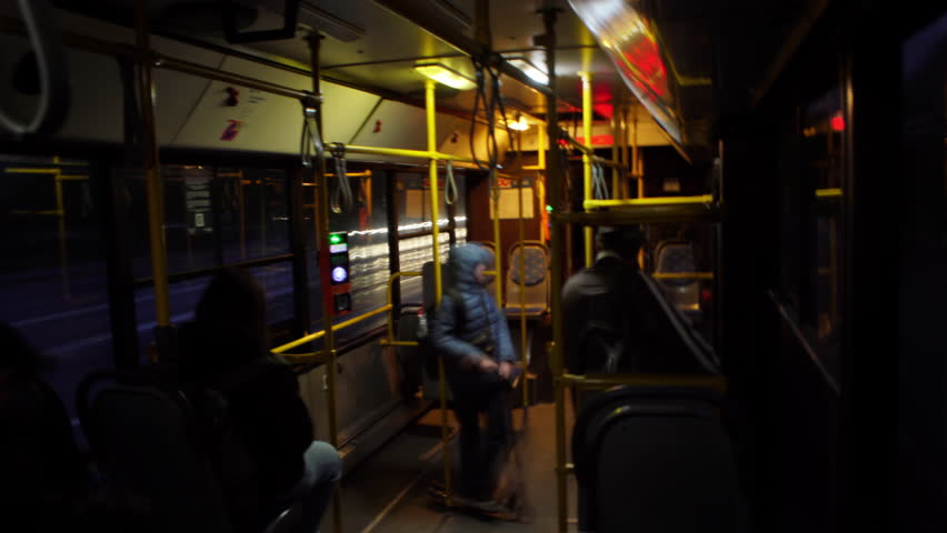 POV timelapse from inside a city bus at dusk; window view captures light trails, motion-blurred people and traffic, showcasing fast-paced urban commute vibe.