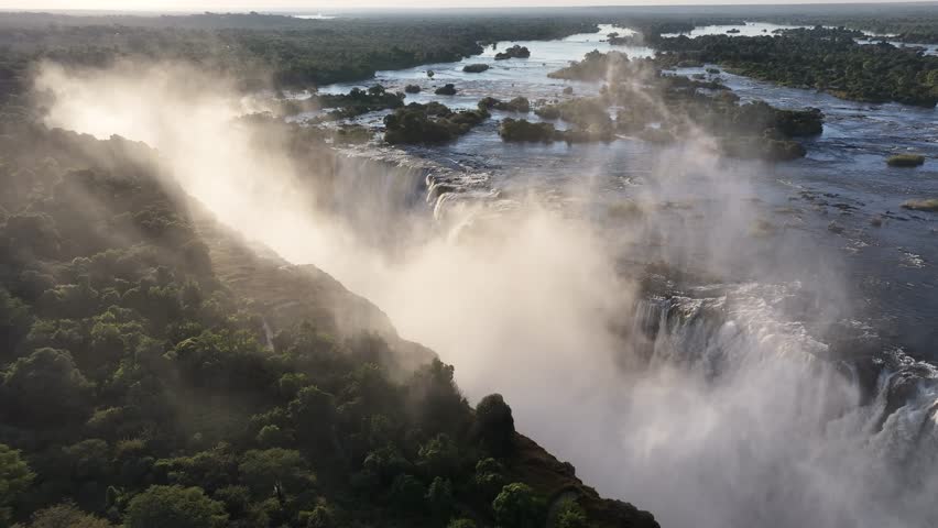 Scenic Water Falls In Victoria Falls Matabeleland North Zimbabwe. Rainbow Forming Over Waterfalls With River In Background. Idyllic Forest Water Falls Beauty. Idyllic Travel Landscape.