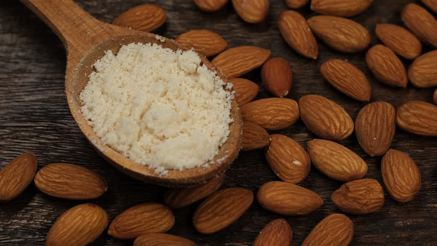 Whole almonds and flour from almonds in spoon on wooden board, rotation