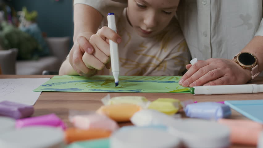 Tilt up shot of caring Caucasian mother assisting teenage boy with cerebral palsy drawing at table in flat