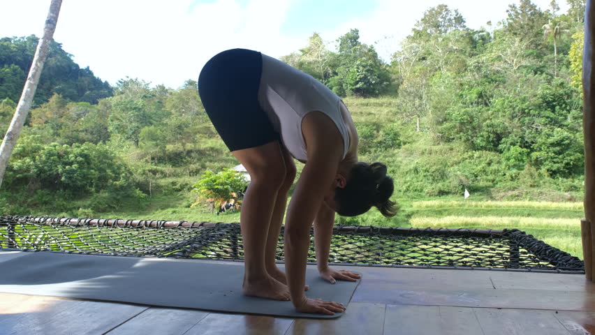 Young woman practicing yoga on a bamboo terrace by the scenic view of tropical greenery and tranquil rice plantations, slow motion. Active lifestyle and wellness concept