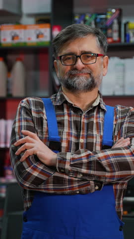 Smiling senior man posing proudly in an auto parts store surrounded by motor oil and car supplies.