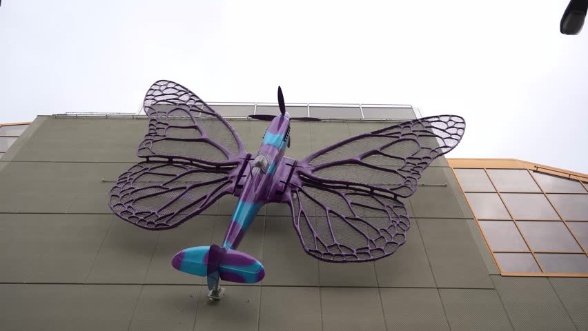 Fantasy aircraft shaped like a butterfly flapping its wings in front of historic architecture in Prague. Surreal fusion of technology and nature in a magical urban setting.

