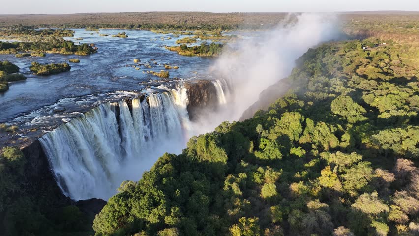 Famous Water Falls In Victoria Falls Matabeleland North Zimbabwe. Rainbow Forming Over Waterfalls With River In Background. Nature Dramatic Sky Mountain Canyon. Nature Outside Panoramic View.