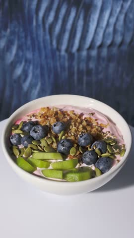 white healthy breakfast bowl with jogurt and fruits turning on  blue background, zoom in, food closeup