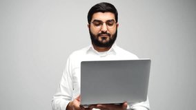 Confident young man in a white shirt holding a laptop stands against a neutral background in a modern setting	
 - Powered by Shutterstock - Get 15% off with code: PIKWIZARD15