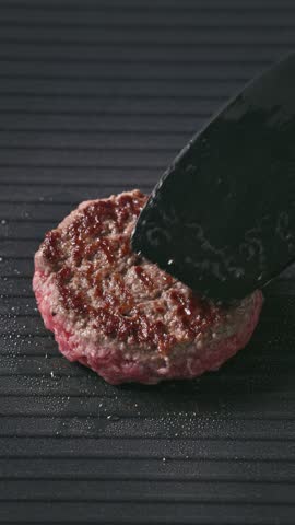 cook turn around minced beef burger meat  cooking on hot black electric grill surface, food closeup