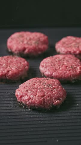 minced beef burger meat patties cooking on hot black electric grill surface, food closeup