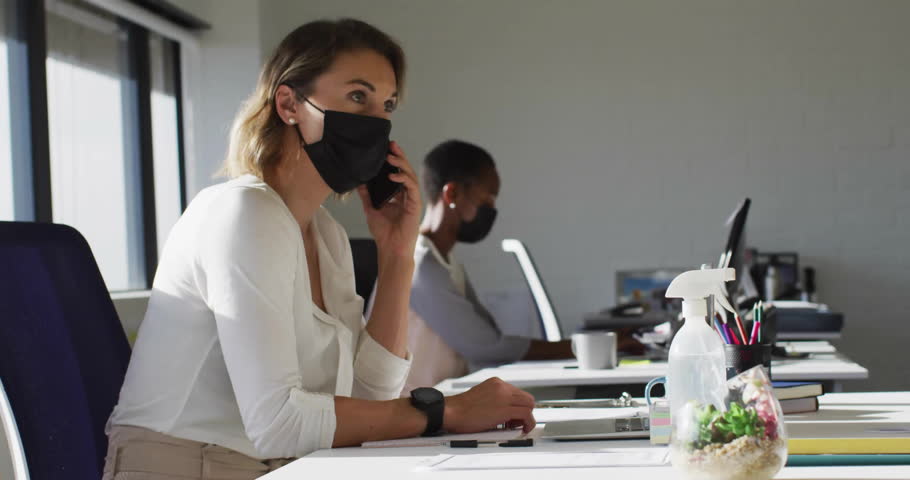 Masked call handler answering phone and animating marketing like comment follower counts at desk. Corporate, communication, collaboration, technology, productivity, modern, professional