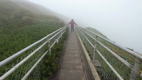 Man walks up steep Point Reyes Lighthouse steps in rain mist and fog. Walking from support building down to lighthouse equal to 30 story building with over 300 steps. Steep climb lots of exercise.
