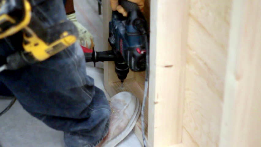 Focused precision as a worker carefully drills into wooden panels, surrounded by sawdust and tools, capturing a moment of silent concentration and craftsmanship.