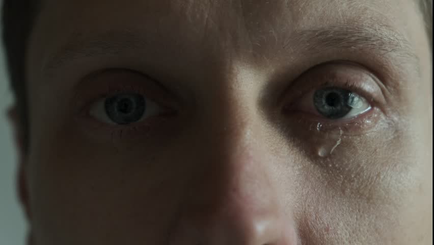 Man's eye with tear drop, extreme close-up. Emotional man with tears streaming down face. Dramatic of guy crying in despair