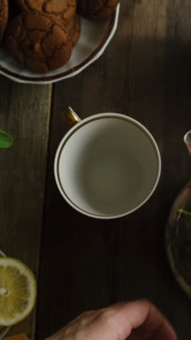 Vertical video. Woman pours herbal green tea from teapot during breakfast. Morning tea ritual