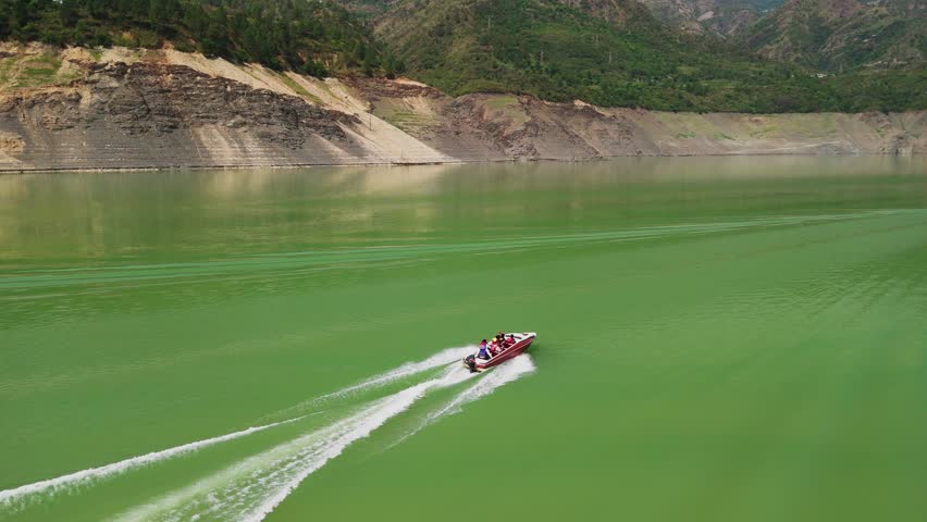 Speedboat cruises across vivid green water with passengers enjoying a scenic ride along rocky hills and forested slopes.